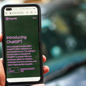 Close-up of a smartphone showing ChatGPT details on the OpenAI website, held by a person.